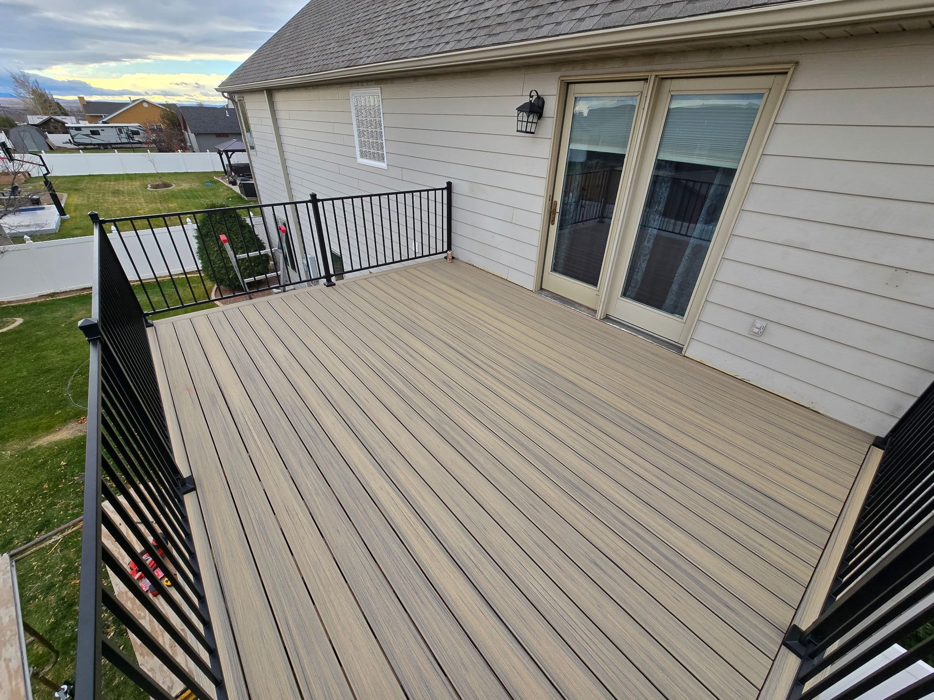Composite deck with black railing, leading to French doors on a beige house.