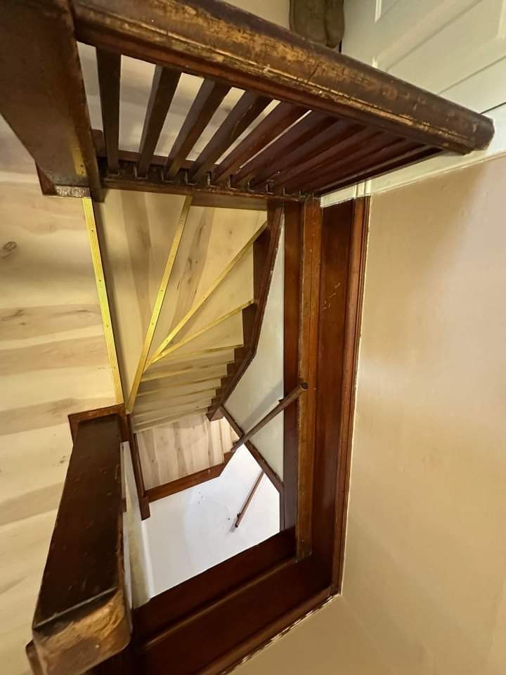 Wooden staircase viewed from above. Brown railing and steps, light-colored walls.