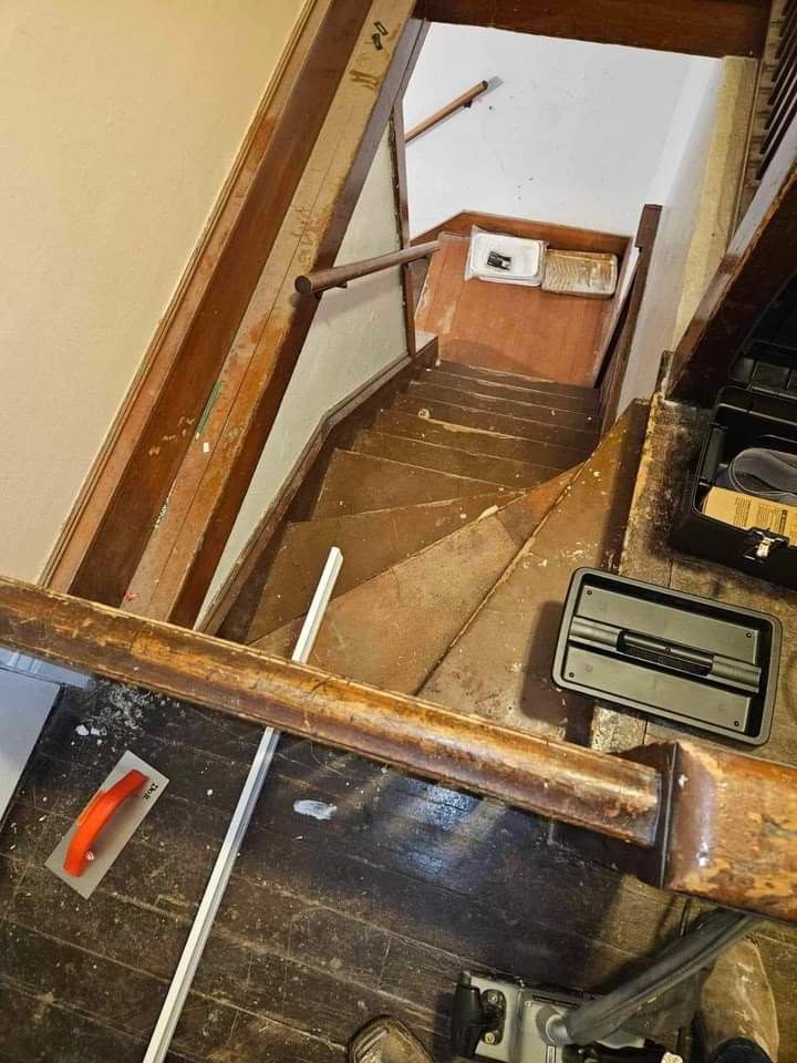 Staircase with worn wooden steps and railing, showing wear and tear. Tools and debris on the floor.