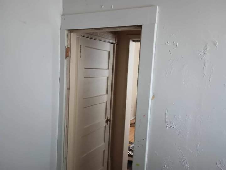 White door frame with open, panel door. Interior room with peeling paint visible.