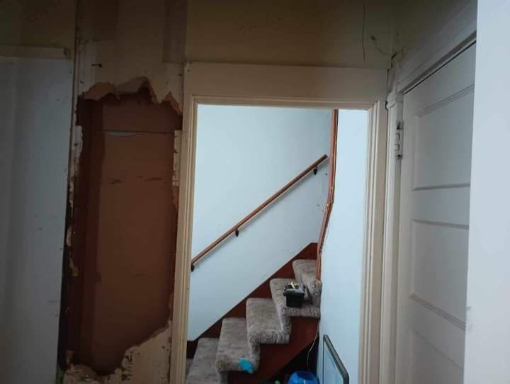 Interior view: doorway to staircase with wall damage on the left.