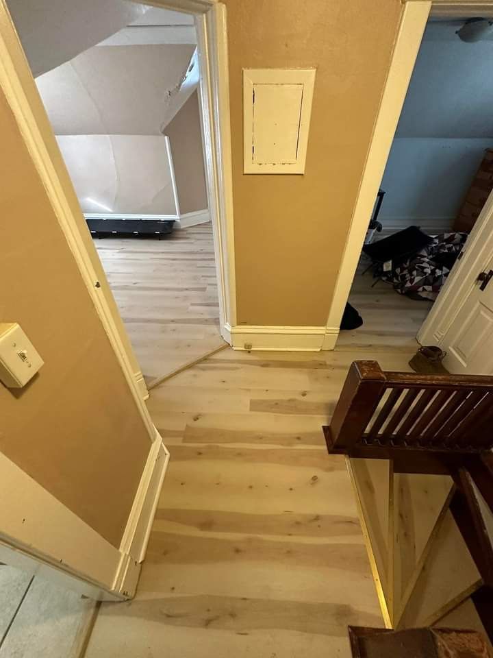 Hallway with light-colored flooring, tan walls, and a wooden stairwell. Doors and electrical panel are visible.