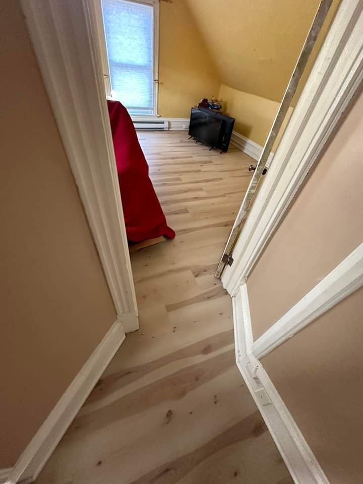 View of a bedroom with light wood floor, bed with red cover, and small window.
