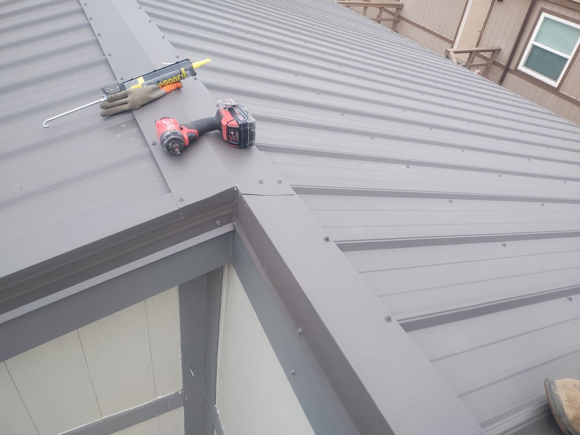 Gray metal roof construction with caulk gun, drill, and trim.