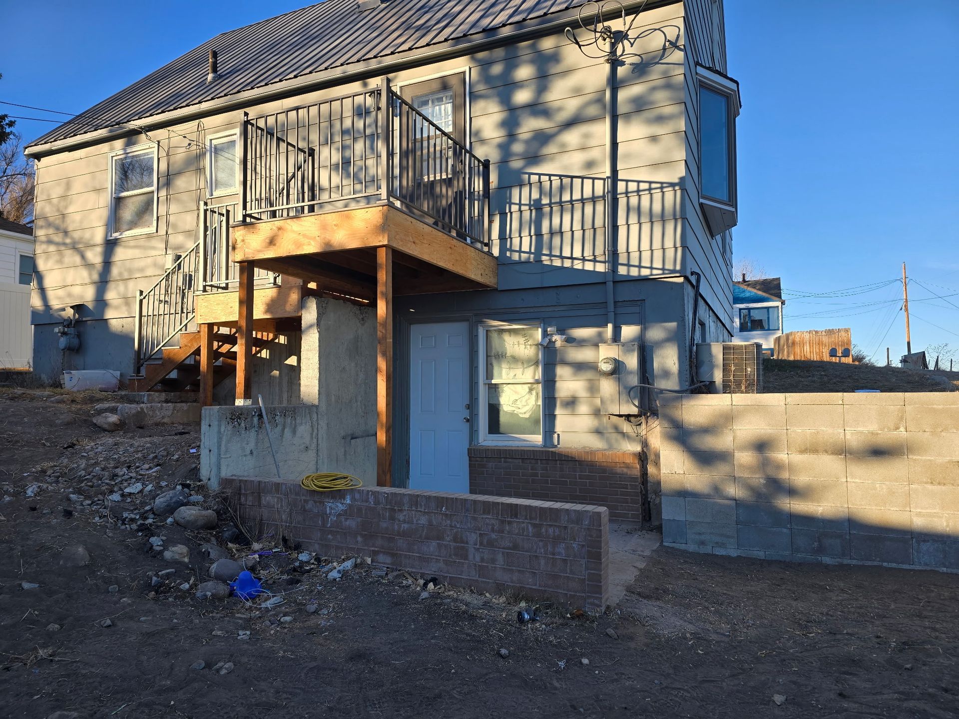 Back of a two-story house with a wooden deck, a concrete foundation, and a small yard with gravel.