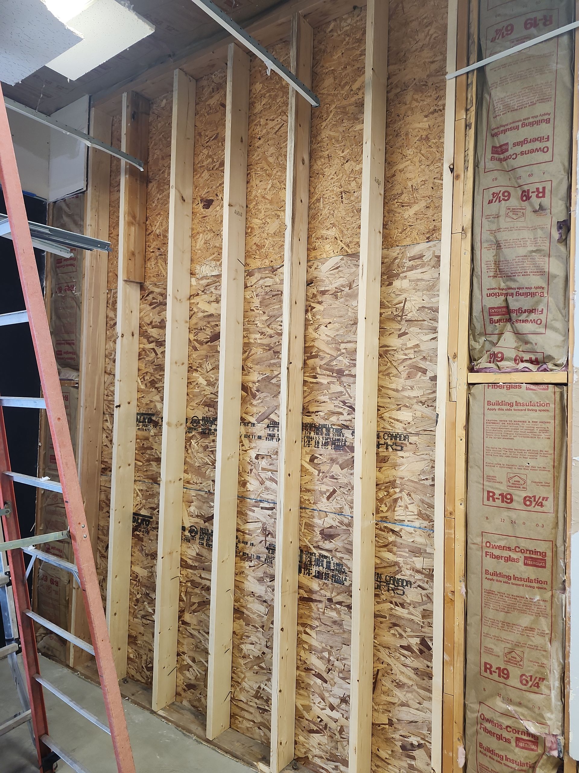 Framing of a wall with wood studs and oriented strand board, with insulation on the right.