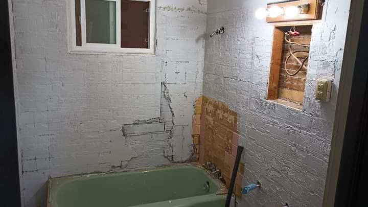 Bathroom under renovation, featuring a green tub, white-painted brick walls with exposed areas, and a small window.