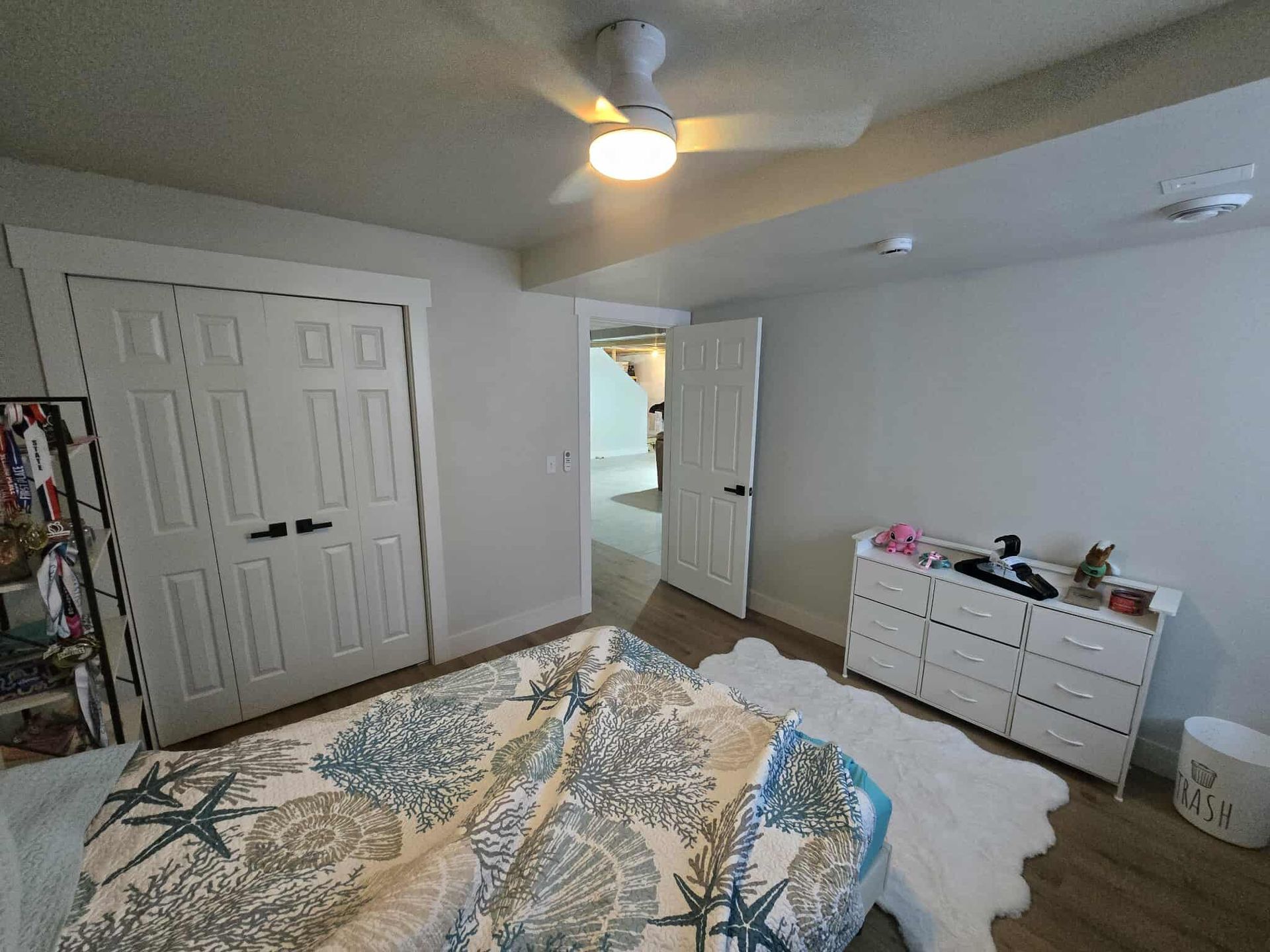 Bedroom with white dresser, closet doors, and bed with blue seashell-patterned quilt.