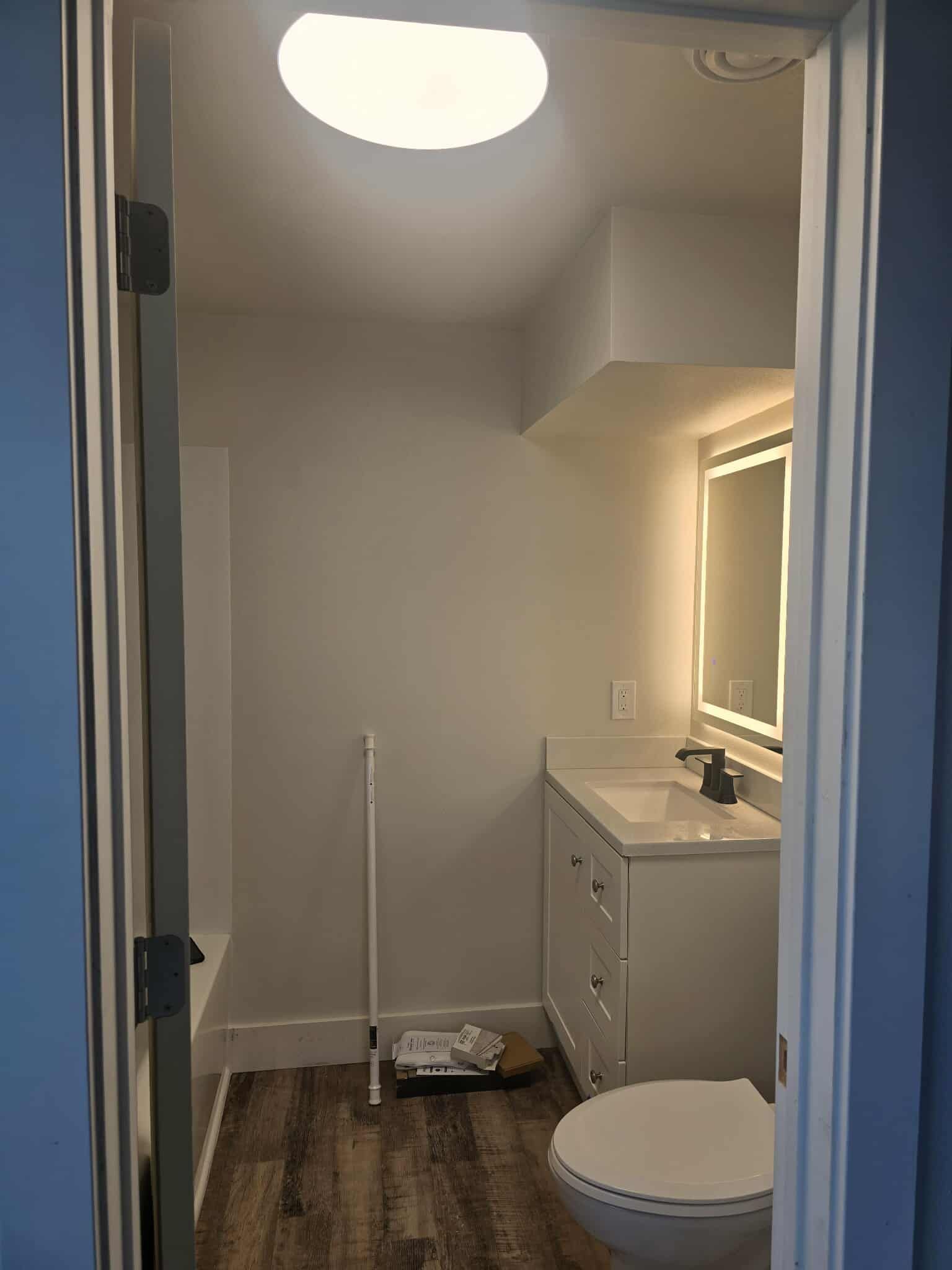 Bathroom interior with white vanity, toilet, and lit mirror; skylight overhead.