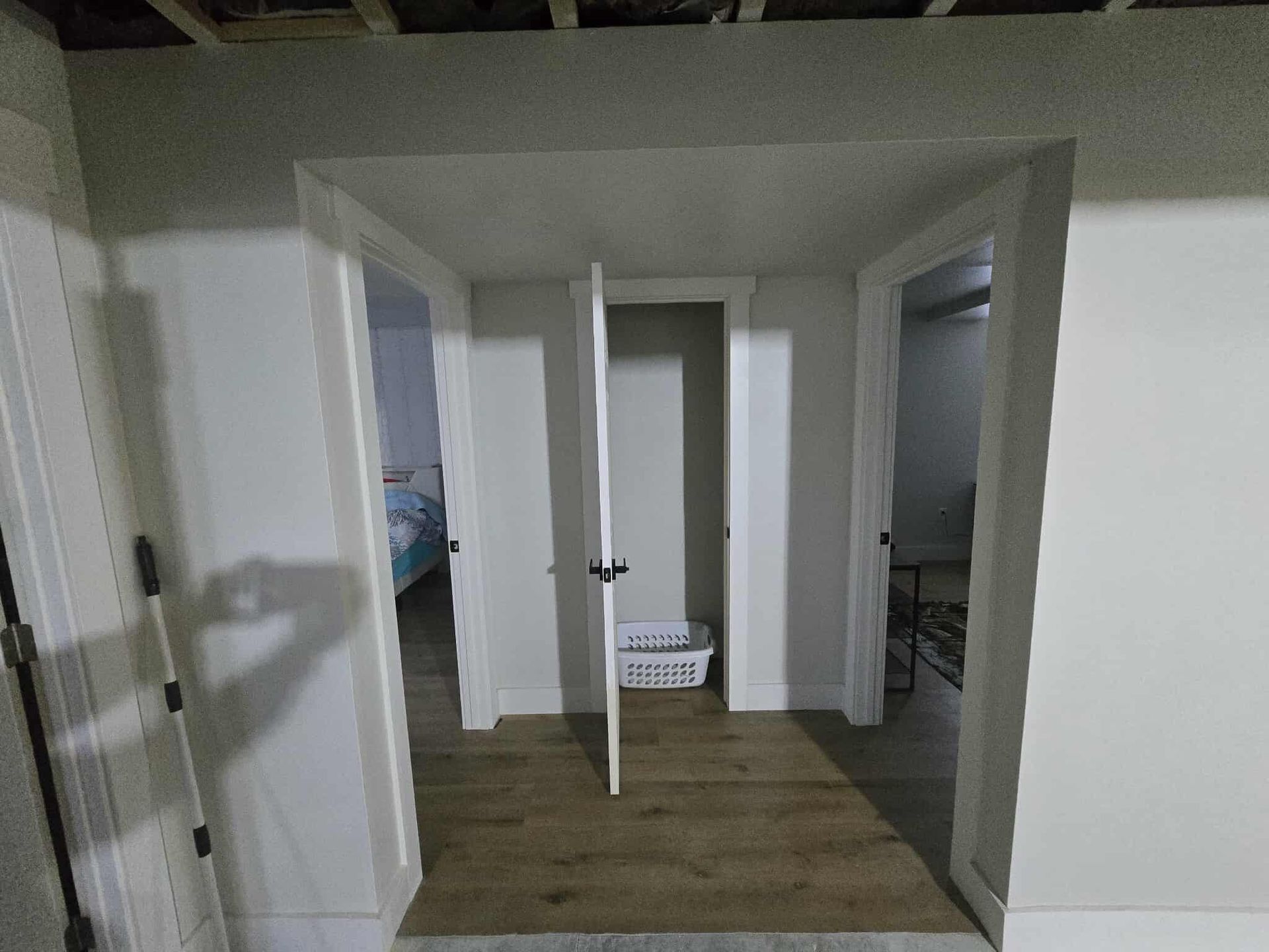 Hallway with three doorways, one open to a closet. White walls, wooden floor.