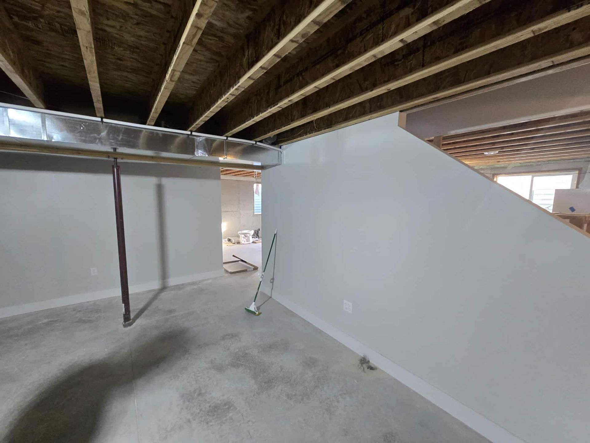 Basement with concrete floor, unfinished ceiling, metal ductwork, and white painted walls.