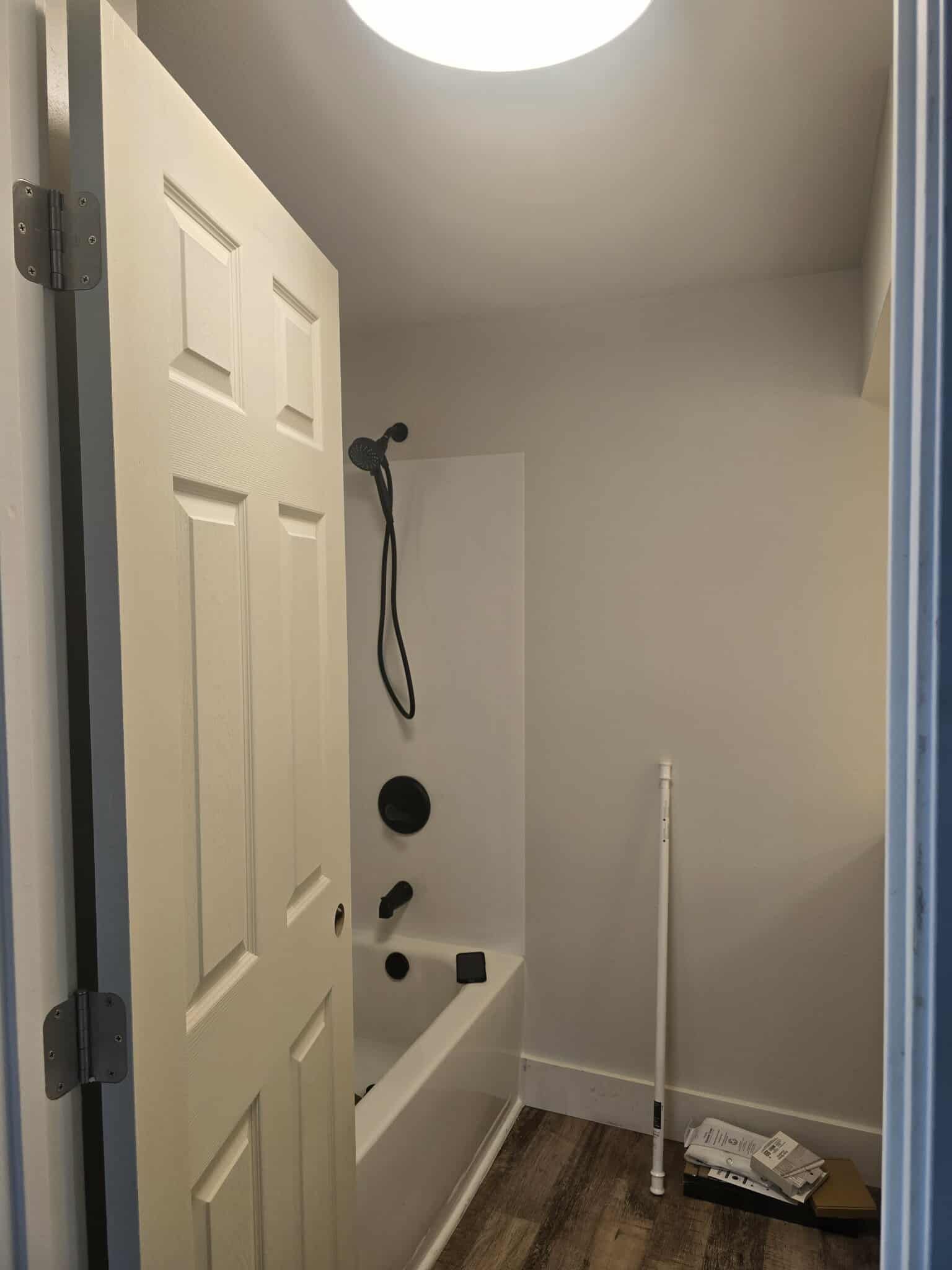 Bathroom with white door open, shower with black fixtures, and light fixture.