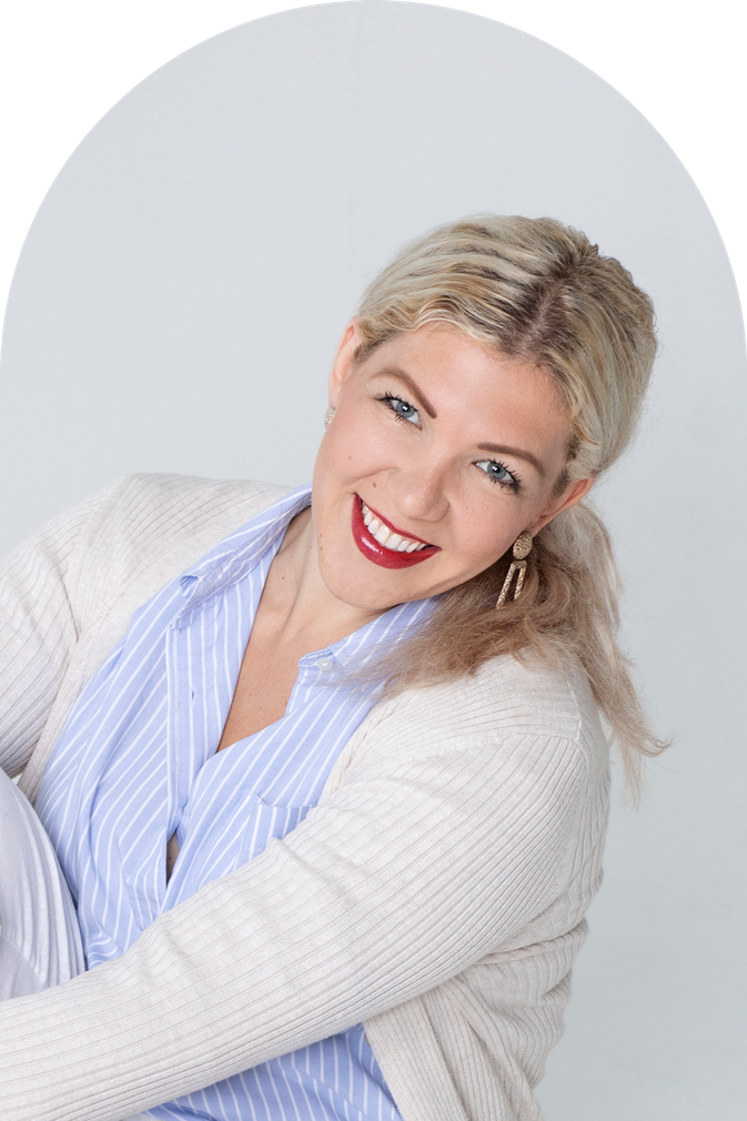 Femme blonde, souriant largement, portant une chemise à rayures bleues et un cardigan crème.