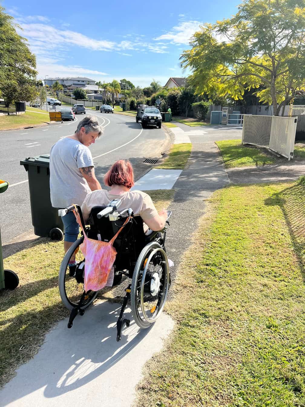 A woman in a wheelchair is walking down a sidewalk next to a man.