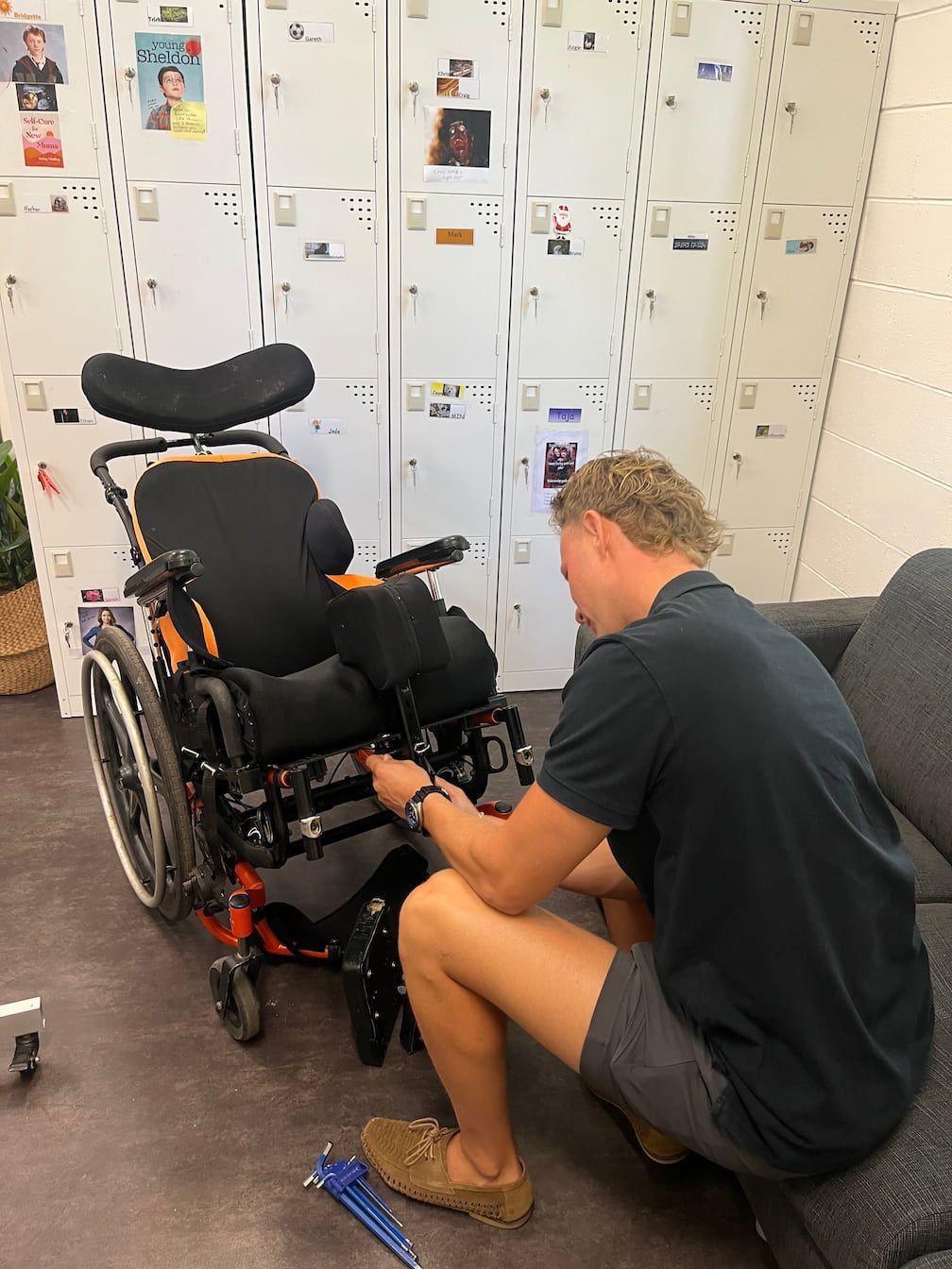 A man is working on a wheelchair in front of lockers.