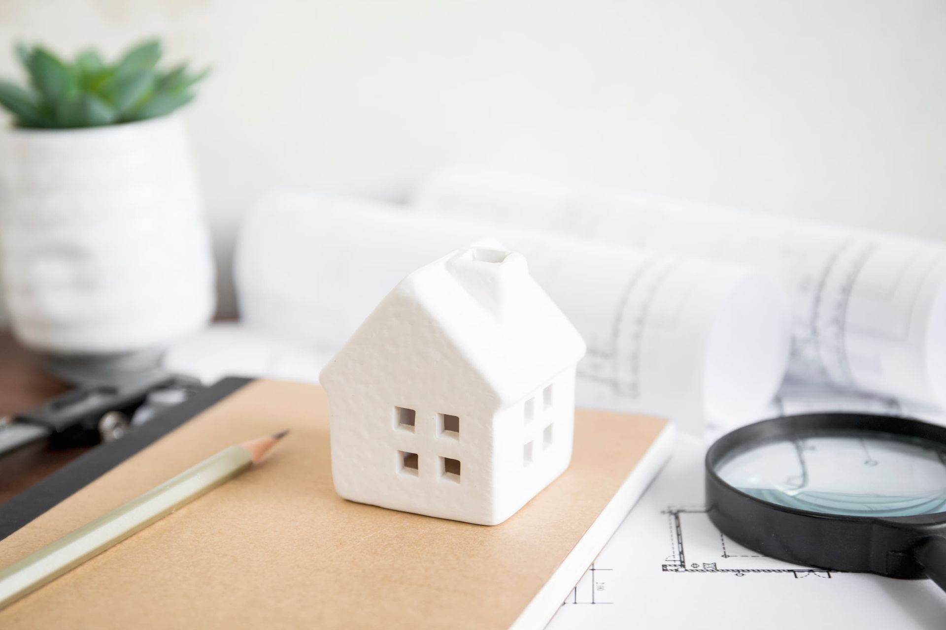 A model house is sitting on top of a notebook next to a magnifying glass.