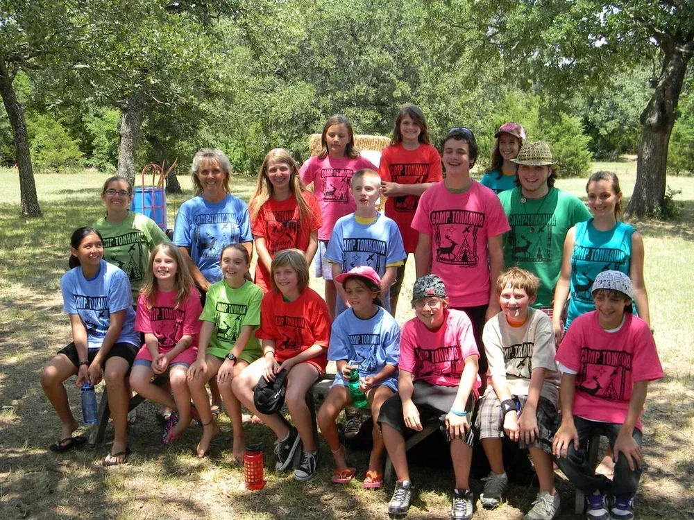 Group of people posing outdoors on a wooded trail, many in bright pink shirts, seated and standing together.