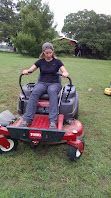 Person seated on a red mobility scooter on a grassy field, smiling with arms resting on the controls.