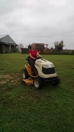 Person riding a yellow riding lawn mower on a grassy yard under a cloudy sky