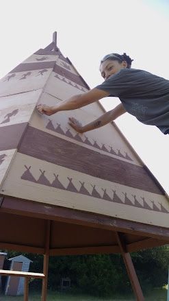 Person placing a patterned panel on a tall outdoor structure under a cloudy sky.