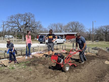 People using a red tiller to dig soil in a community garden on a sunny day