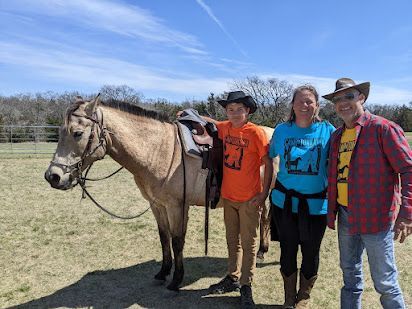Three people standing beside a saddled horse in a sunny field