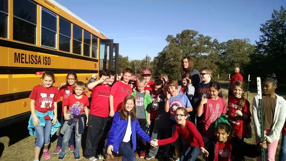 Group of children posing in front of a yellow school bus on a sunny day