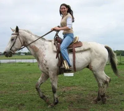 Person riding a white horse on a grassy field under a cloudy sky