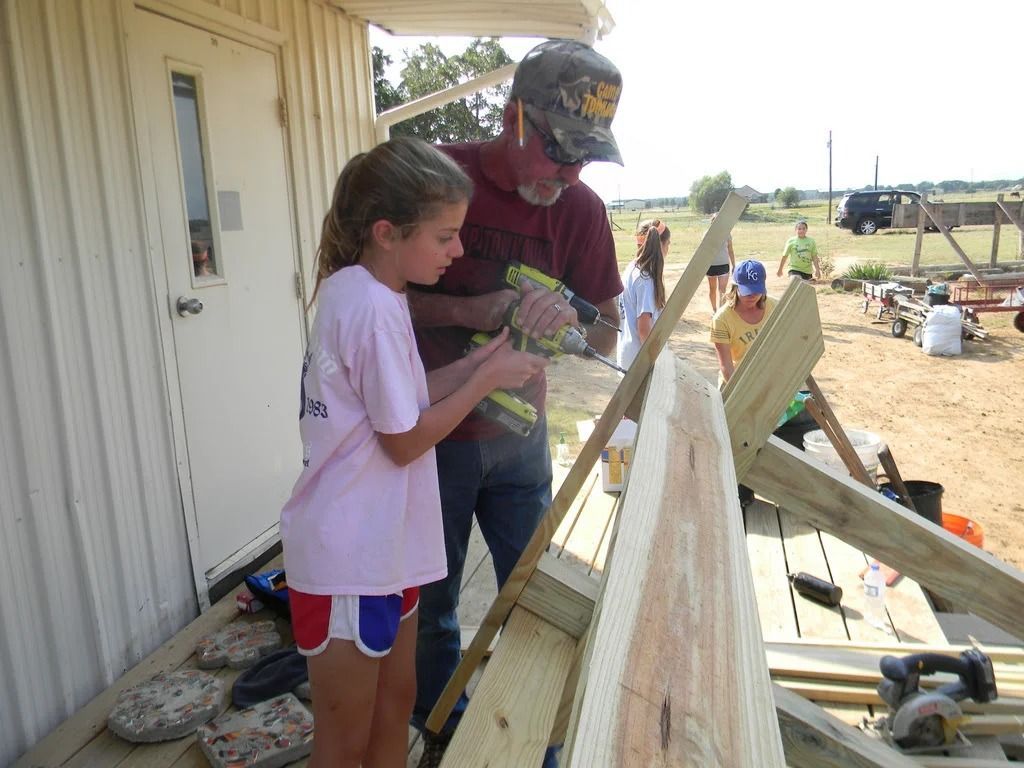 Two people measuring and working on a wooden ramp beside a white building outdoors