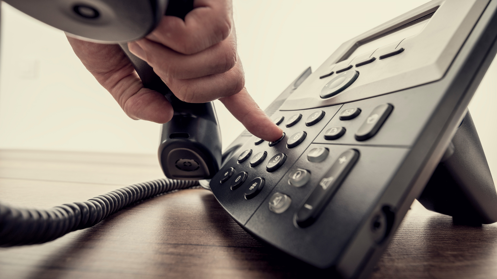 Hand dialing a number on a black office telephone.