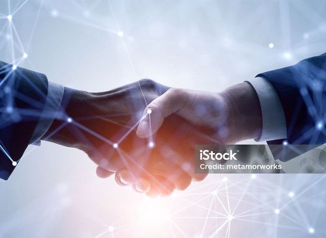 A handshake between two people in business suits, overlaid with a digital, glowing network of connected dots and lines.