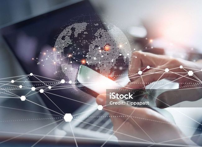 Hands holding a smartphone in front of a laptop, overlayed with a glowing digital globe and a network connection graphic.