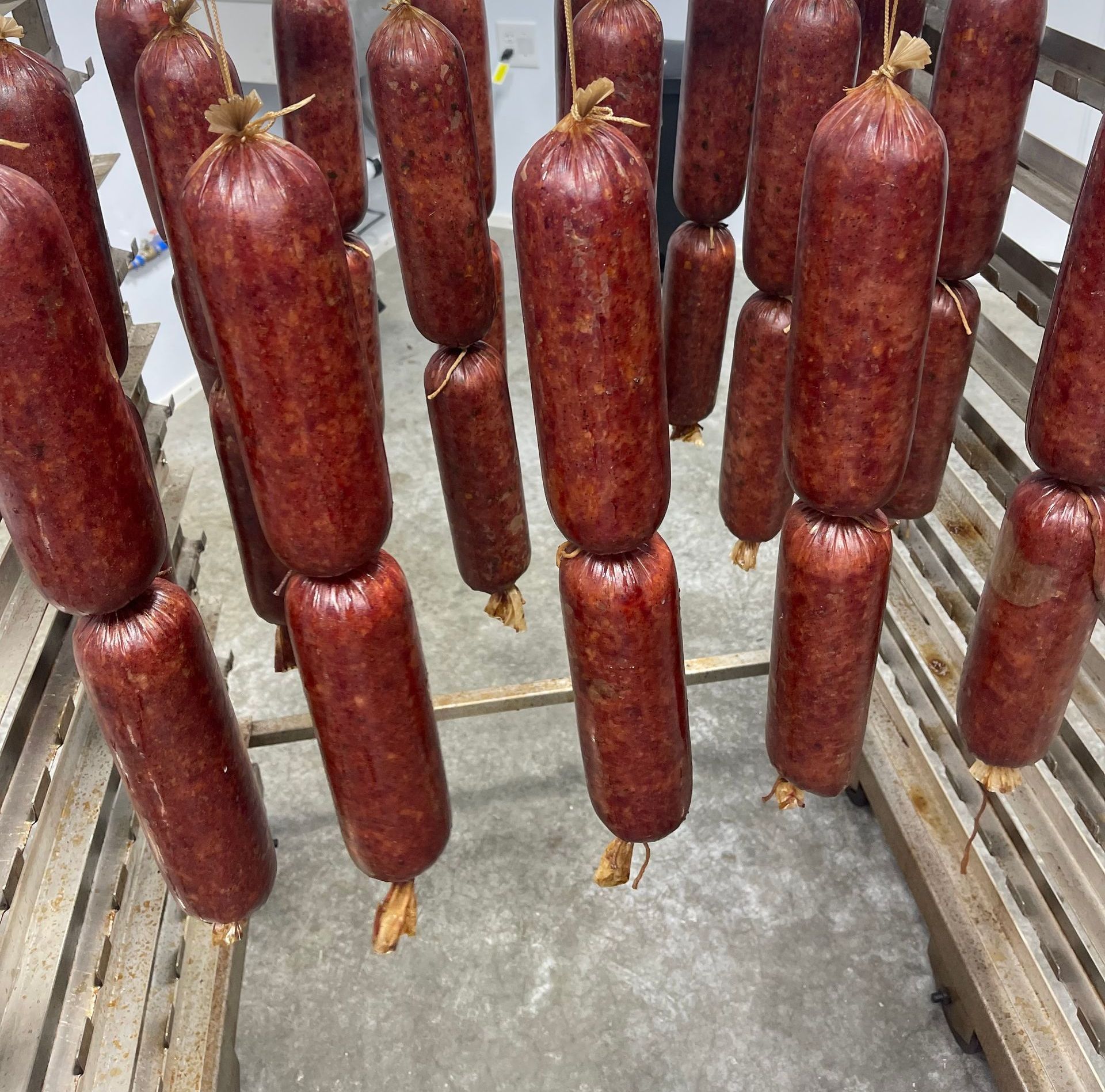 Sausages hanging from a rack in a food production setting. The sausages are dark red/brown.