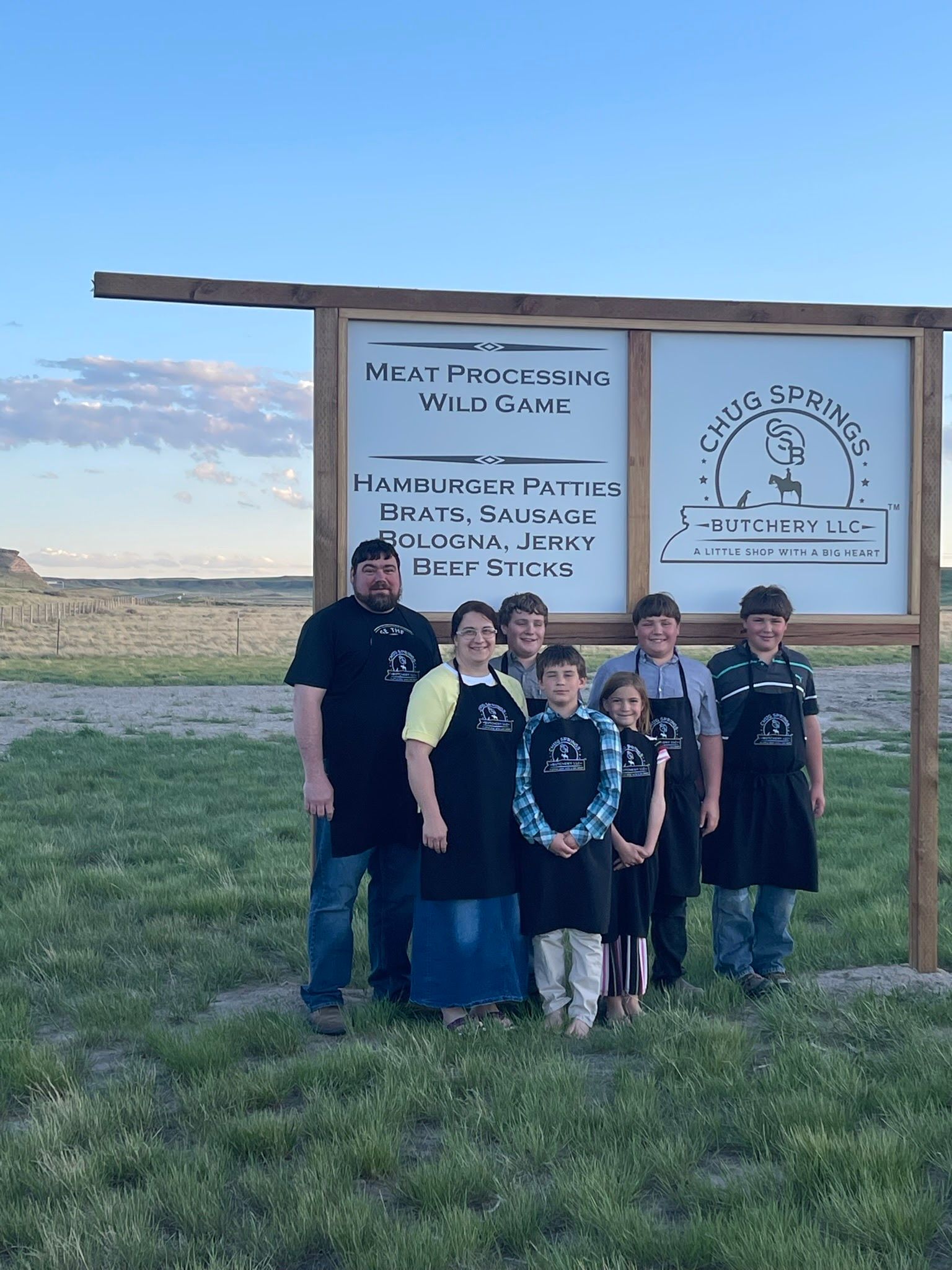 A group of people standing in front of a sign in a field.