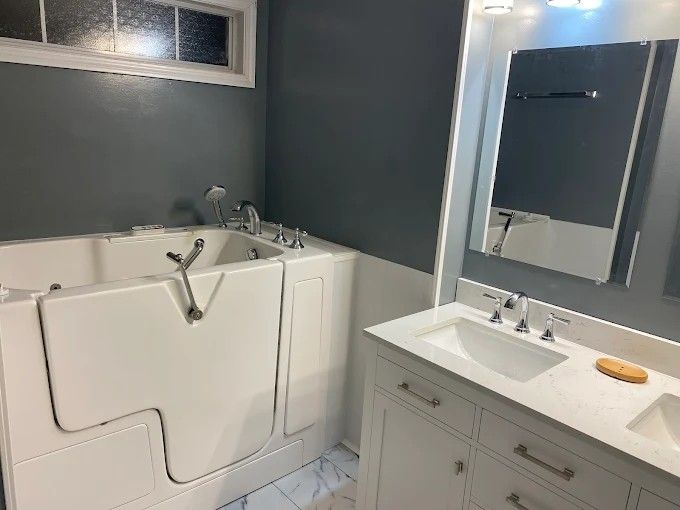 A bathroom with a walk in tub , sink and mirror.