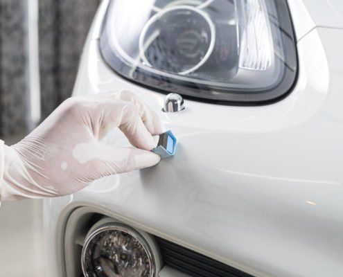 Eine Person mit Handschuhen poliert die Front eines weißen Autos.