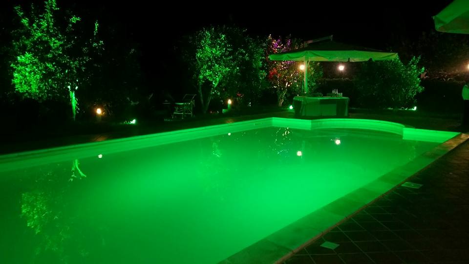 Piscina illuminata di verde di notte, con giardino e gazebo sullo sfondo.
