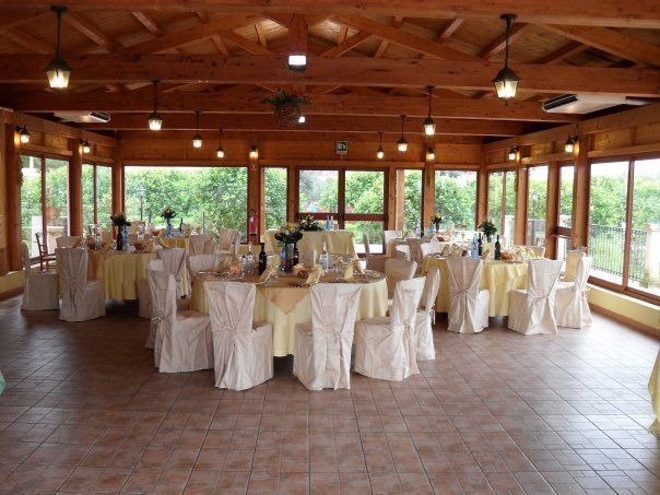 Una sala per banchetti luminosa con tavoli rotondi apparecchiati per un evento formale. Tovaglie gialle, coprisedie bianchi e ampie finestre.