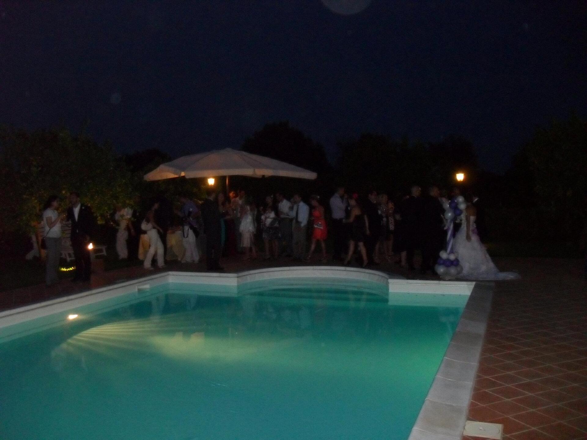 Invitati a un ricevimento di nozze notturno vicino a una piscina; la sposa in abito da sposa, gente che socializza.