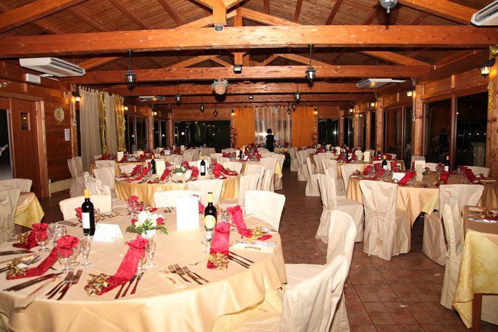 Sala da pranzo del ristorante allestita per una festa, con tavoli rotondi, tovaglie color crema e dettagli rossi.