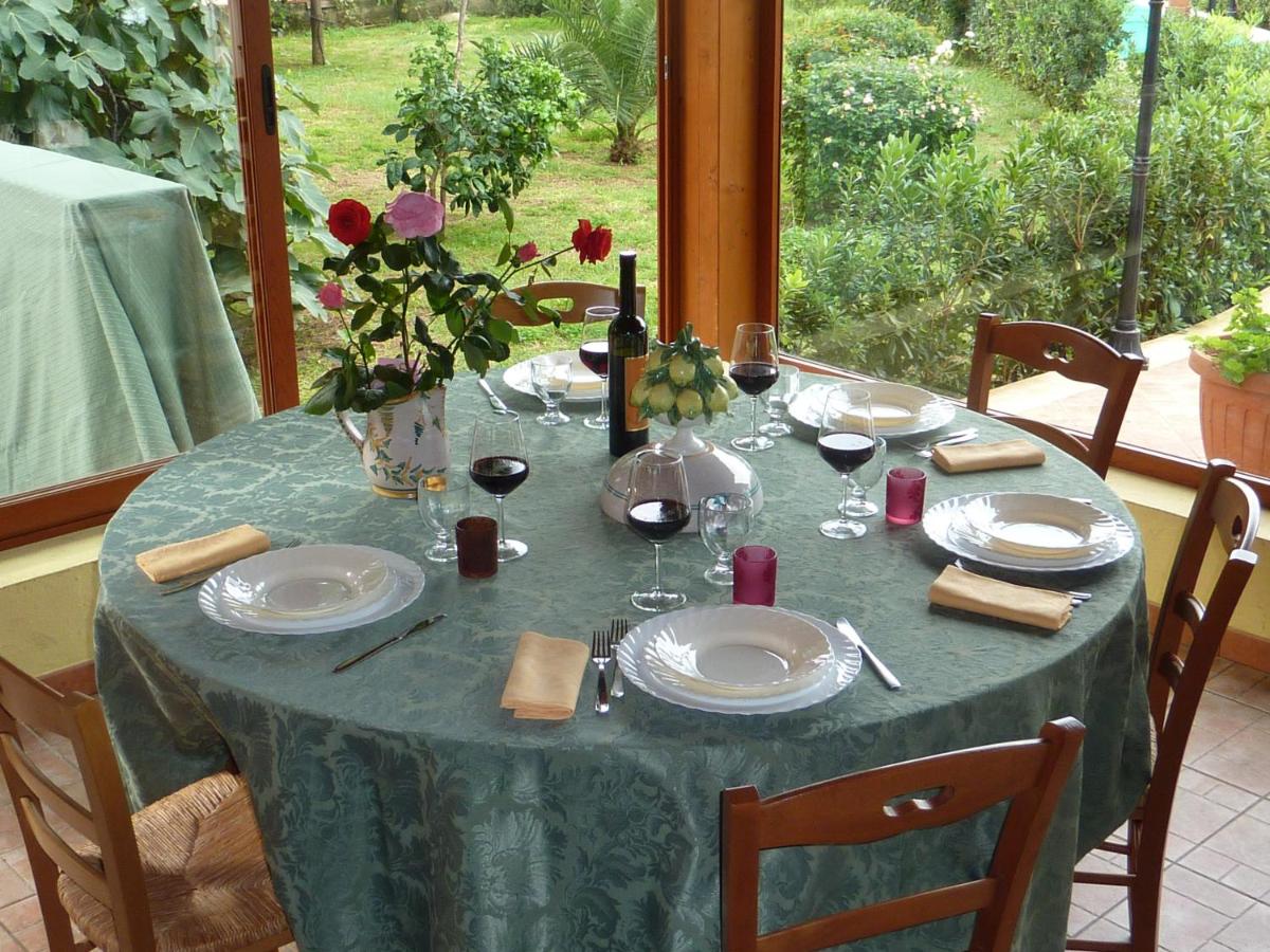 Un tavolo rotondo apparecchiato per un pasto, in una veranda, con una tovaglia verde e vista sul giardino.