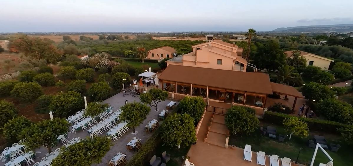 Vista aerea di una location per matrimoni con tavoli, alberi ed edifici in un ambiente rurale.