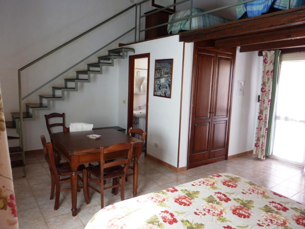 Interno di una stanza con tavolo da pranzo, scale per il soppalco, ampio armadio e letto con biancheria floreale.