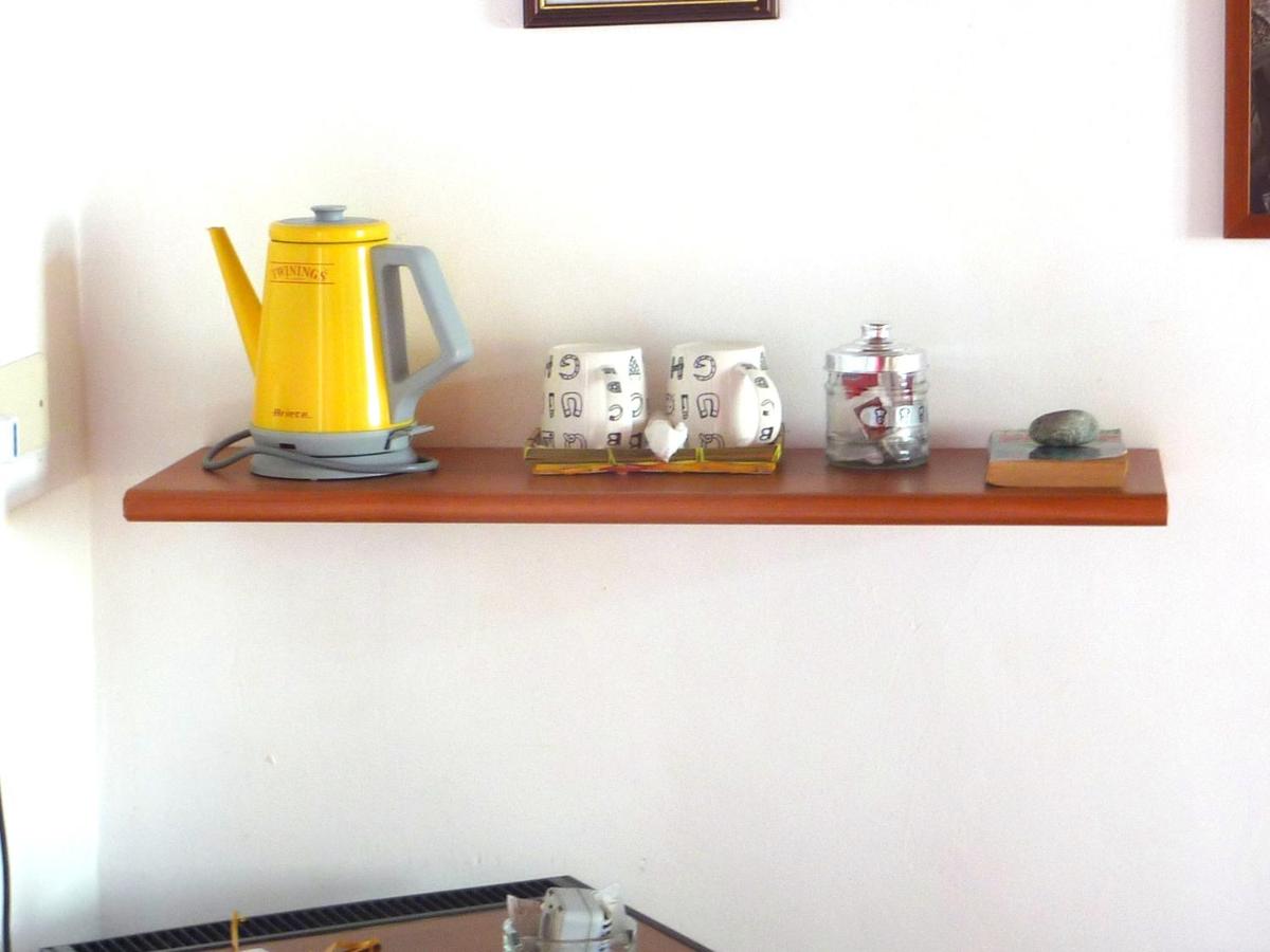 Una mensola di legno su una parete bianca con un bollitore elettrico giallo, tazze e oggetti decorativi.