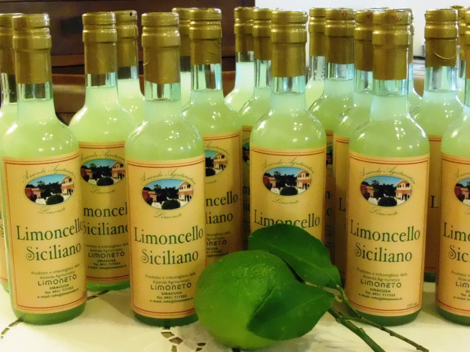 Bottiglie di Limoncello Siciliano con lime, tappi dorati ed etichetta.