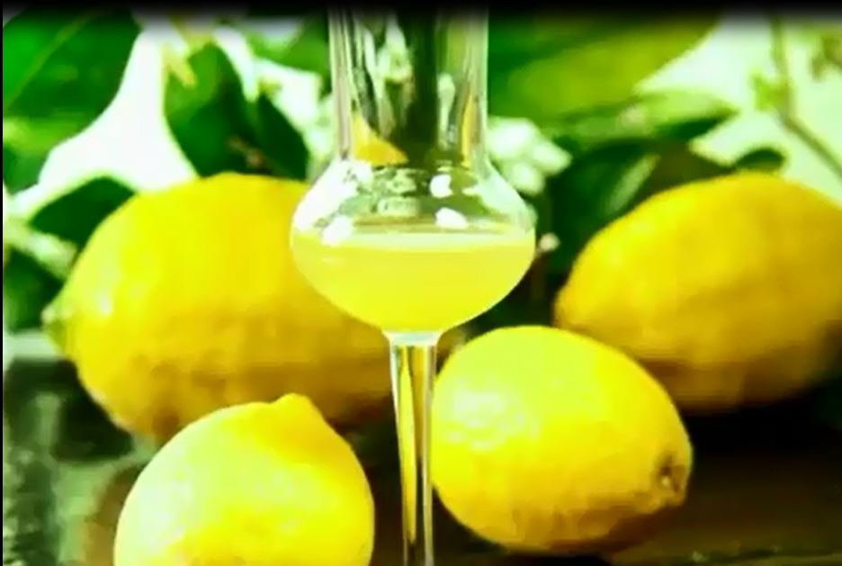 Limoncello in un bicchiere con stelo circondato da limoni.