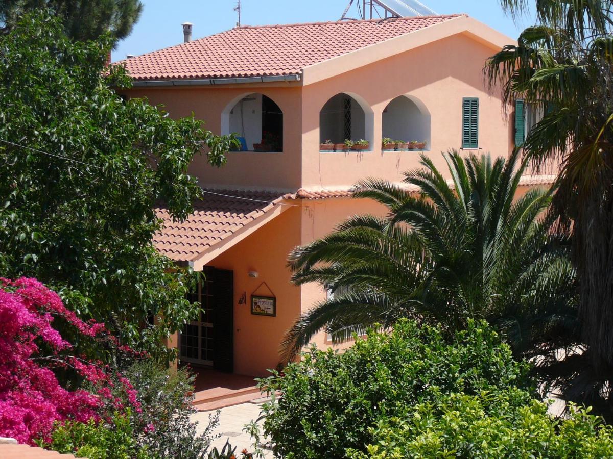 Casa a due piani color pesca con tetto di tegole rosse, finestre ad arco e lussureggiante vegetazione verde in un ambiente soleggiato.