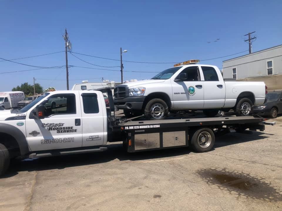 White tow truck carrying a white pickup truck. Both are in an outdoor lot, on a sunny day.