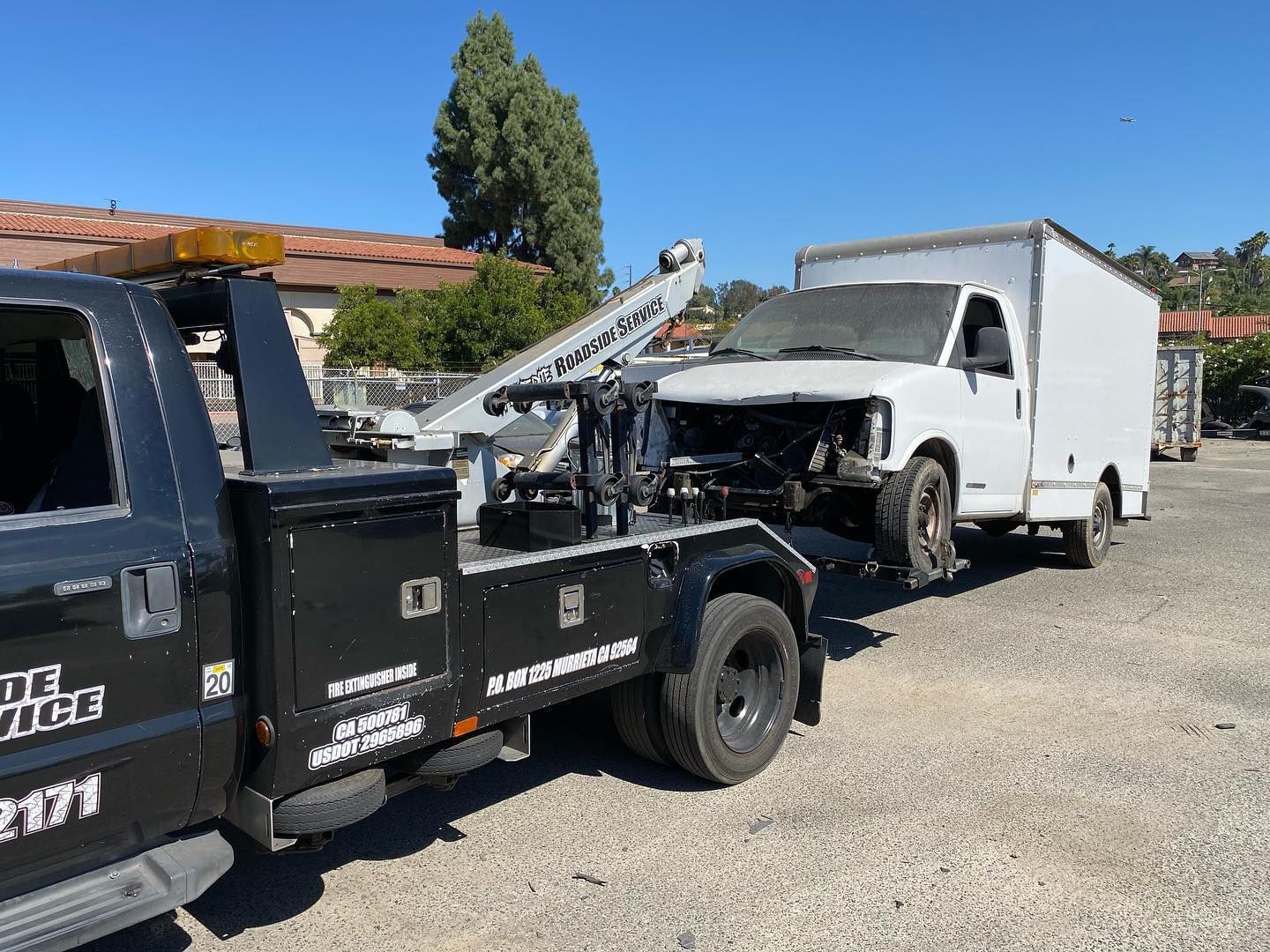 Tow truck towing a damaged white box truck on a sunny day.