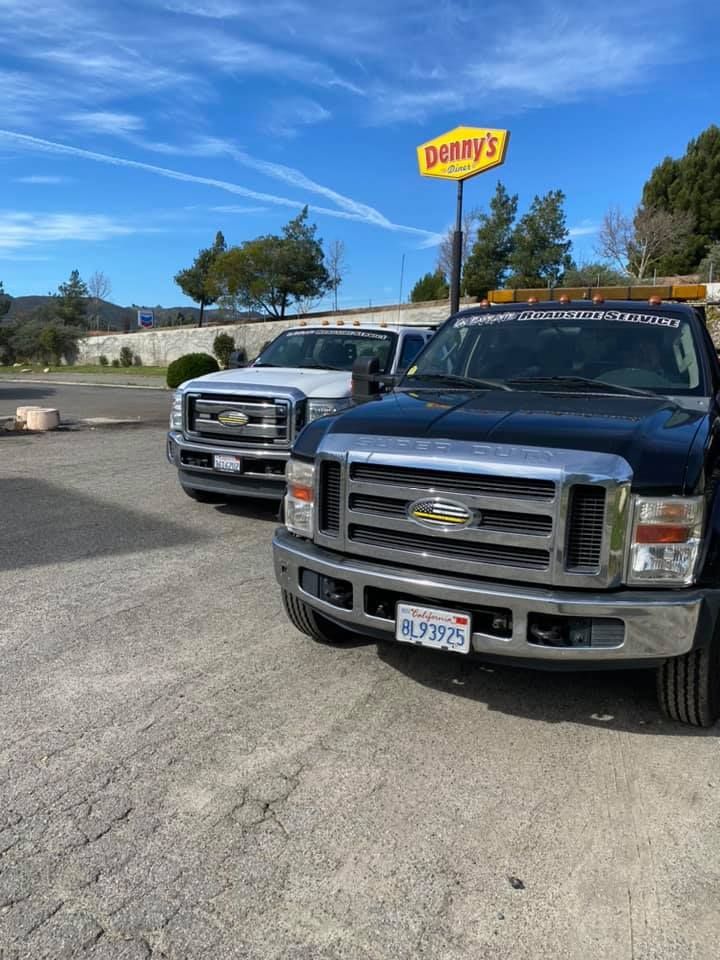Two tow trucks parked in front of a Denny's restaurant on a sunny day.